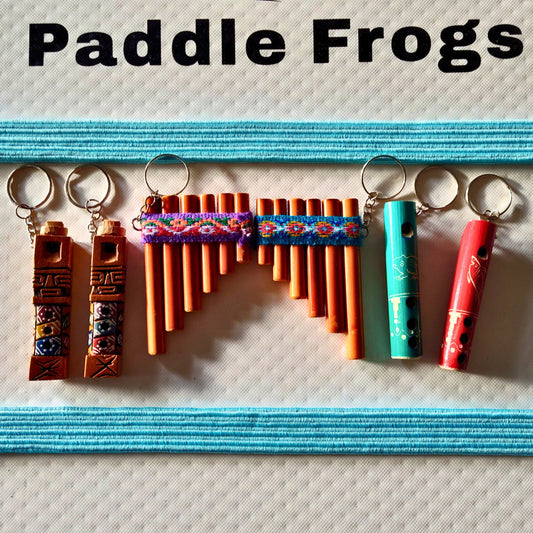 Colorful musical instruments keychains on a textured paddle board surface with 'Paddle Frogs' text above.